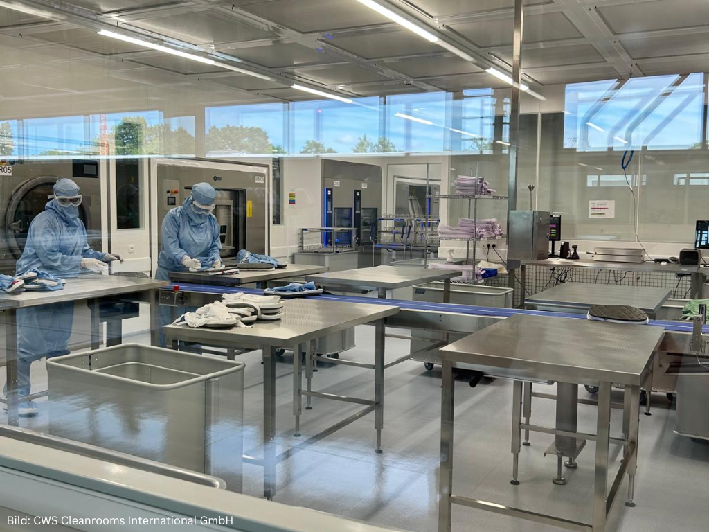 Moderne Reinraum-Fertigungsanlage mit Edelstahl-Arbeitsplätzen und Mitarbeitenden in Schutzkleidung für hygienische Produktionsprozesse und höchste Qualitätsstandards.